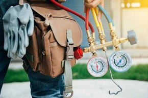 Technicien en combinaison bleue et gants rouges effectuant la maintenance d'une chaudière murale dans un local technique